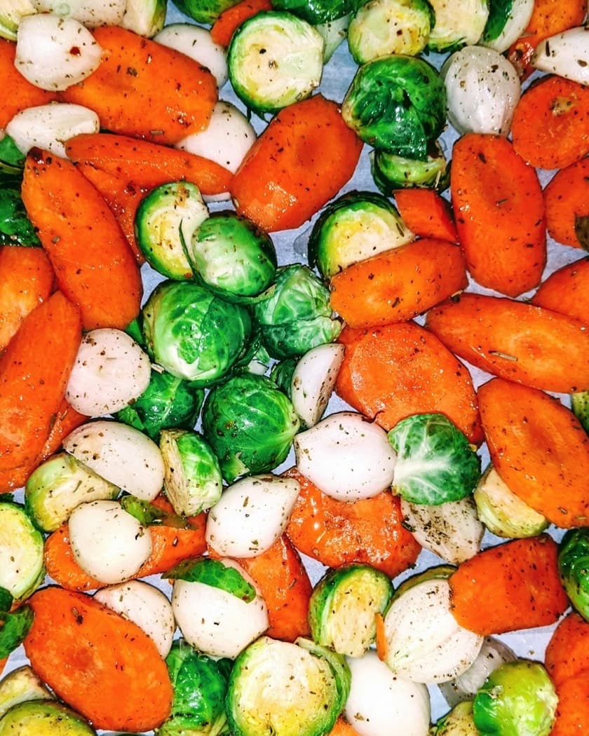 Sliced carrots, onion and halved Brussels sprouts spread out together, seen from above.