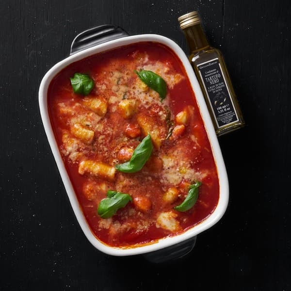 Gnocchi baked in tomato sauce with basil leaves in a white dish, olive oil bottle alongside.